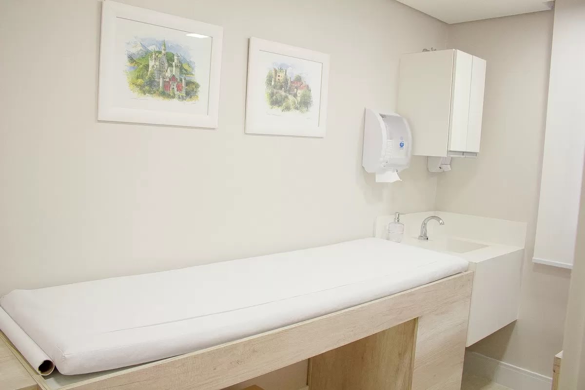 Sala de exame dermatológico, com maca, pia e bancada de apoio